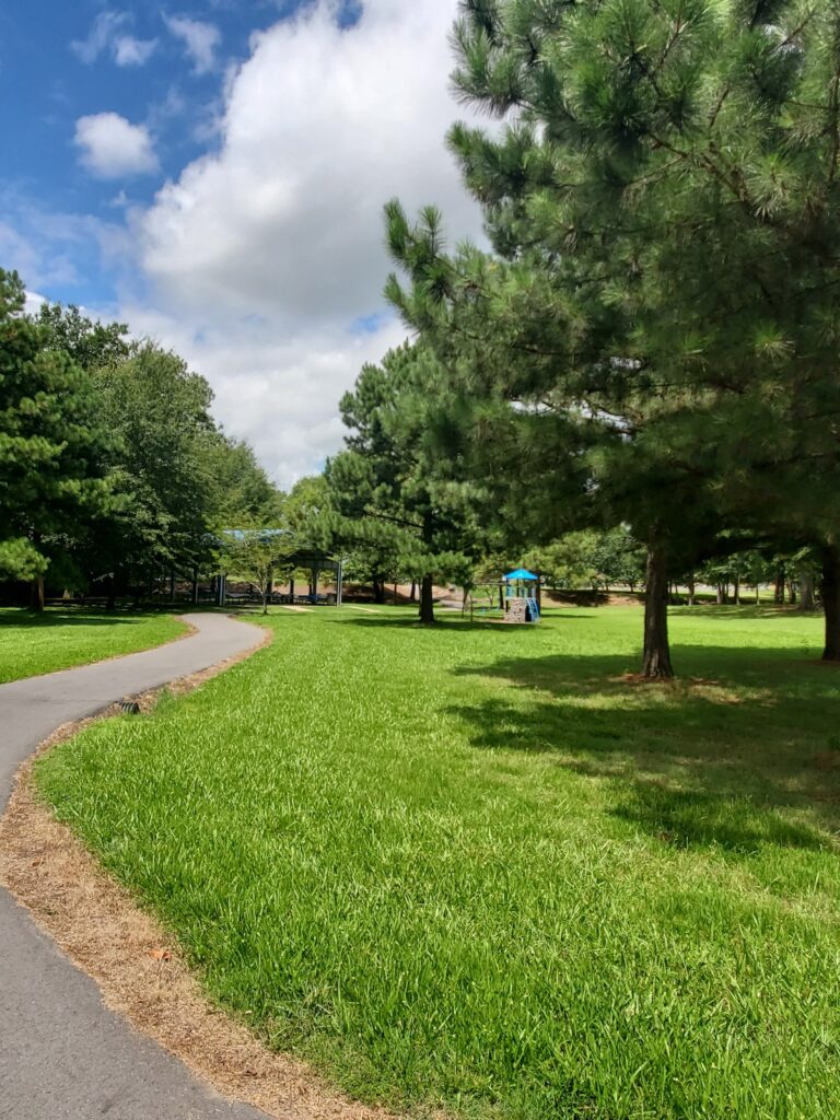 A walking trail winding through a green park. A small blue play area can be seen on the side.