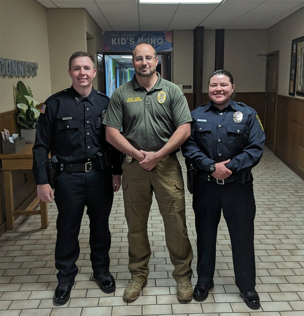 Three police officers posing in the hallway of a church.