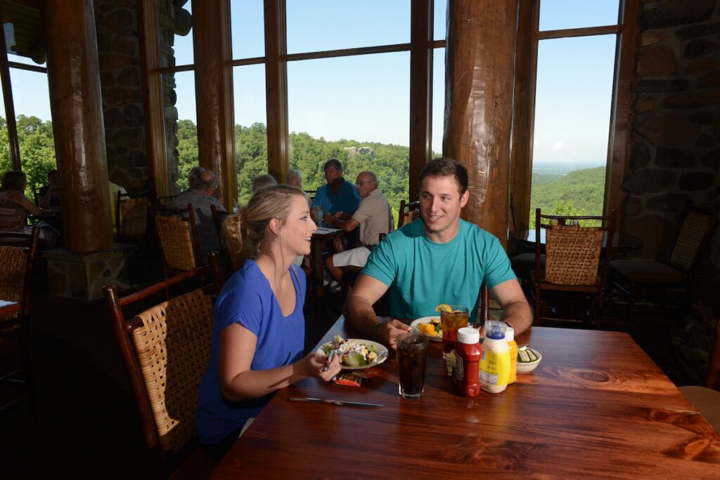 A couple eating salads for lunch in Mather Lodge. Behind them a view of the Petit Jean can be seen from the windows.
