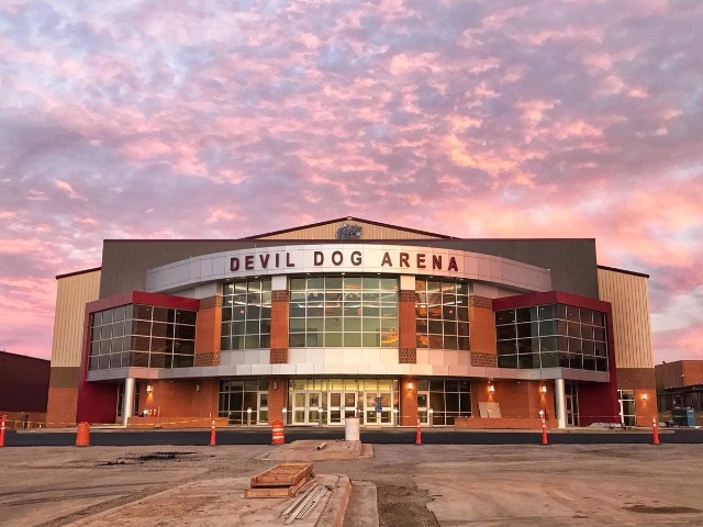 The Devil Dog Arena at sunset. The sky is full of scattered pink clouds. The front of the arena is mostly made of windows.