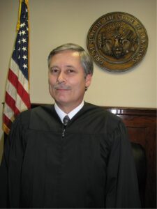 A headshot of the District Court Judge of Morrilton. He is an older white man with gray hair and a mustache.