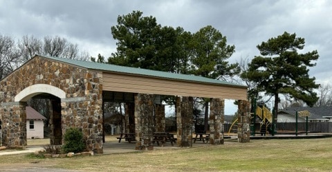 A stone pavilion in a small park. There are multiple separate picnic tables in the pavilion.
